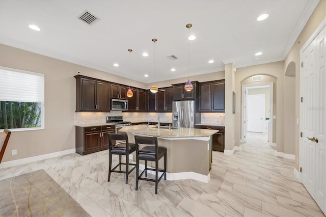 kitchen with appliances with stainless steel finishes, decorative light fixtures, light stone countertops, dark brown cabinets, and a center island with sink