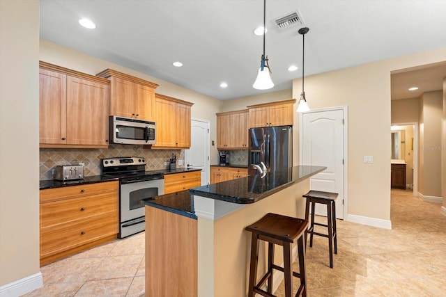 kitchen featuring appliances with stainless steel finishes, a kitchen bar, decorative light fixtures, dark stone countertops, and a center island with sink