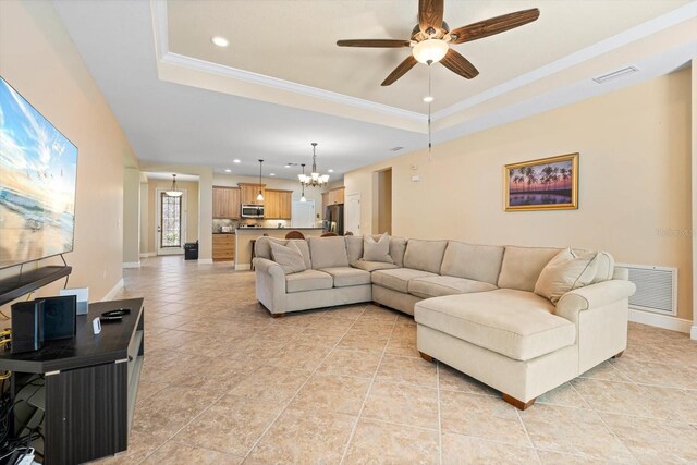 tiled living room with ornamental molding, a tray ceiling, and ceiling fan with notable chandelier