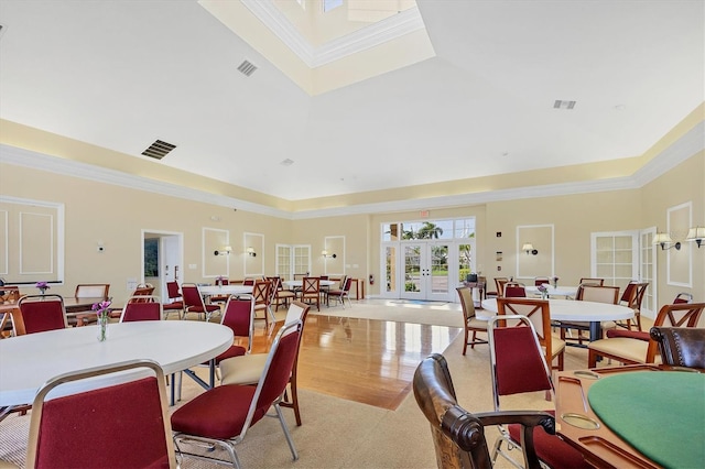 dining space featuring french doors, crown molding, light wood-type flooring, and a towering ceiling