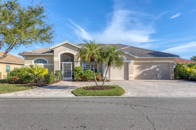 view of front of home featuring a tiled roof, decorative driveway, an attached garage, and stucco siding