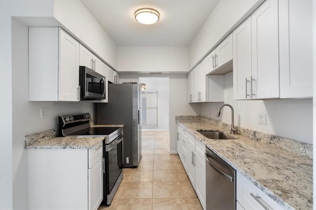 kitchen with sink, light tile patterned floors, light stone counters, white cabinets, and appliances with stainless steel finishes