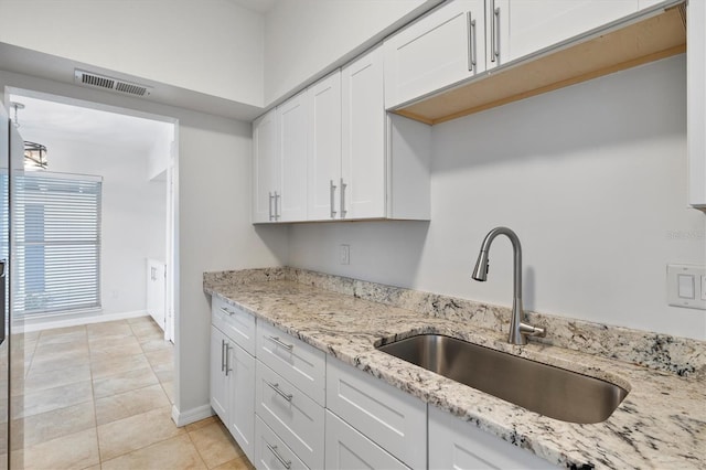 kitchen with light stone countertops, light tile patterned floors, white cabinetry, and sink