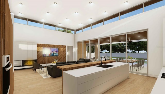 kitchen featuring white cabinets, a towering ceiling, sink, a fireplace, and light wood-type flooring