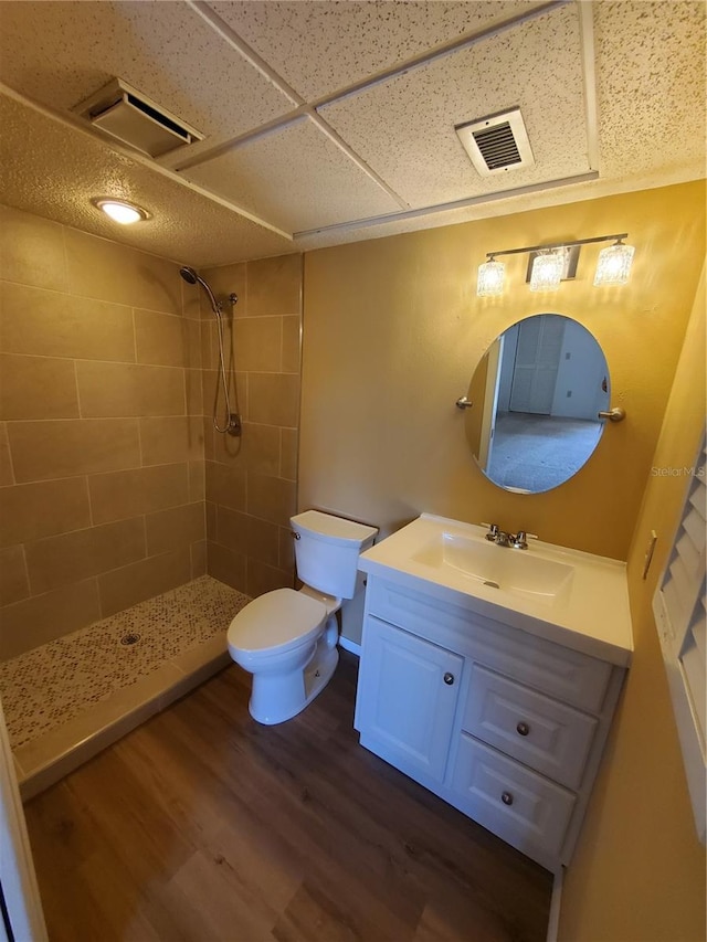 bathroom with a tile shower, hardwood / wood-style floors, vanity, and toilet