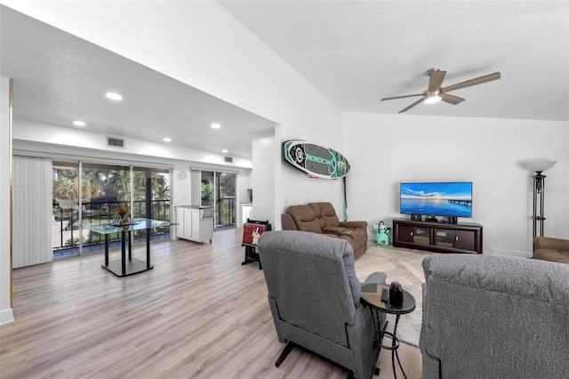 living room with ceiling fan, a textured ceiling, vaulted ceiling, and light wood-type flooring