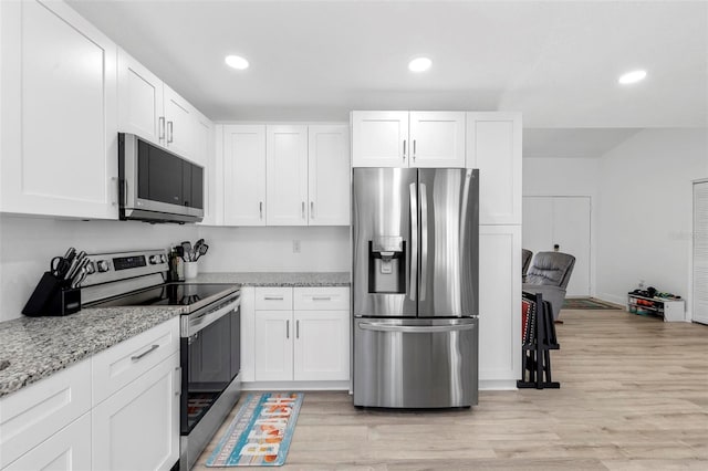 kitchen with light hardwood / wood-style floors, appliances with stainless steel finishes, light stone counters, and white cabinets