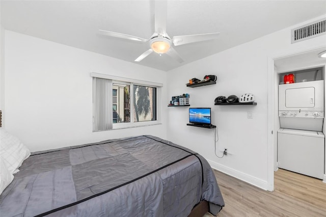 bedroom featuring stacked washer and dryer, light wood-type flooring, and ceiling fan