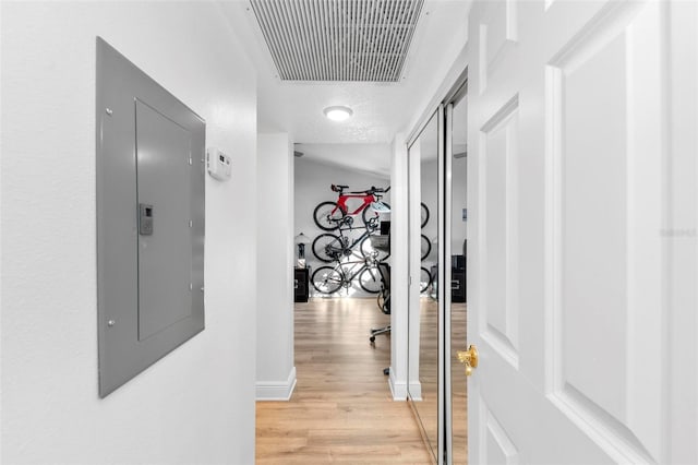 hallway featuring electric panel, light hardwood / wood-style flooring, and a textured ceiling