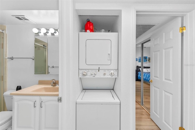 laundry room with stacked washing maching and dryer, sink, and light wood-type flooring