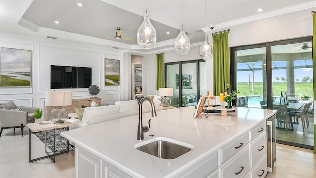 kitchen with a raised ceiling, white cabinetry, a kitchen island with sink, and sink