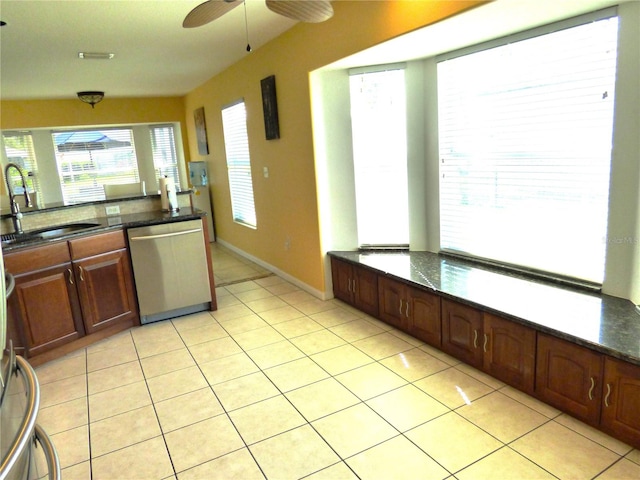 kitchen featuring stainless steel dishwasher, ceiling fan, sink, light tile patterned floors, and dark stone countertops