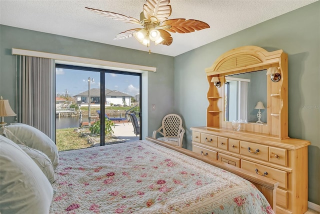 bedroom featuring a textured ceiling, access to exterior, a water view, and ceiling fan