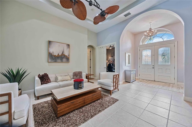 entryway with a raised ceiling, ceiling fan with notable chandelier, and light tile patterned floors