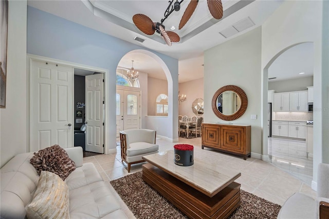 living room with a tray ceiling, ceiling fan with notable chandelier, and light tile patterned floors