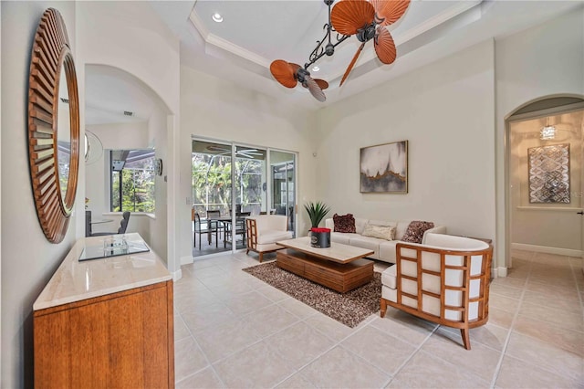 tiled living room with a high ceiling, ornamental molding, ceiling fan, and a tray ceiling