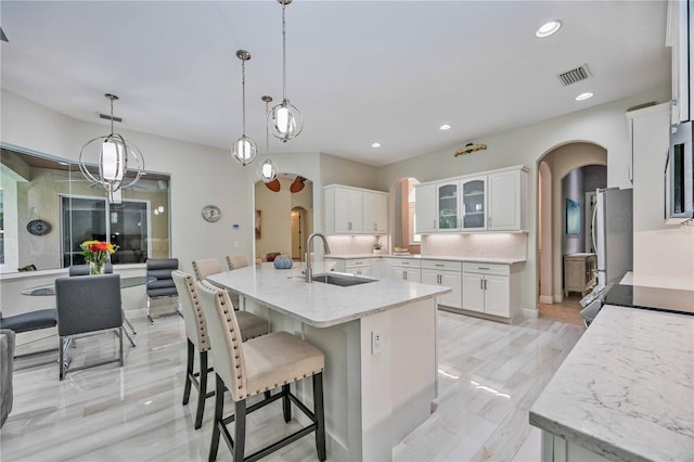 kitchen featuring an island with sink, sink, stainless steel fridge, white cabinets, and hanging light fixtures