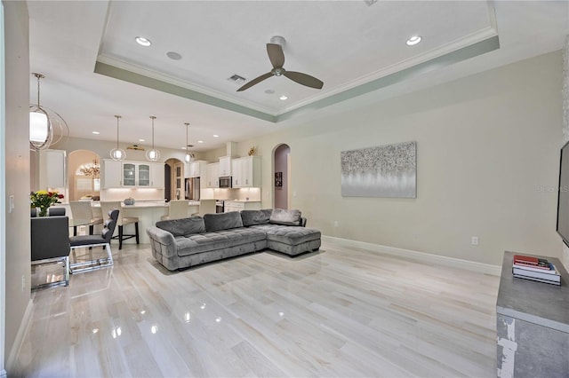 living room with a raised ceiling, ornamental molding, ceiling fan, and light hardwood / wood-style flooring