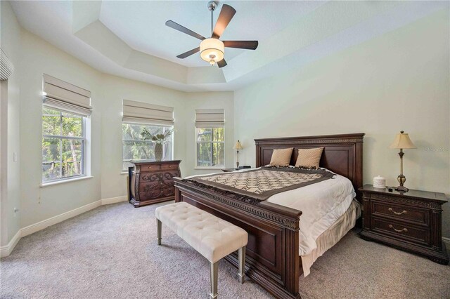 bedroom featuring multiple windows, light colored carpet, a raised ceiling, and ceiling fan