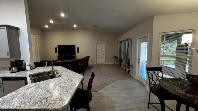 kitchen featuring dishwasher, sink, vaulted ceiling, light stone counters, and a kitchen island with sink