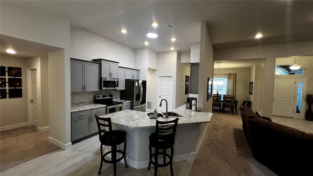 kitchen with gray cabinetry, appliances with stainless steel finishes, sink, a kitchen breakfast bar, and a center island with sink