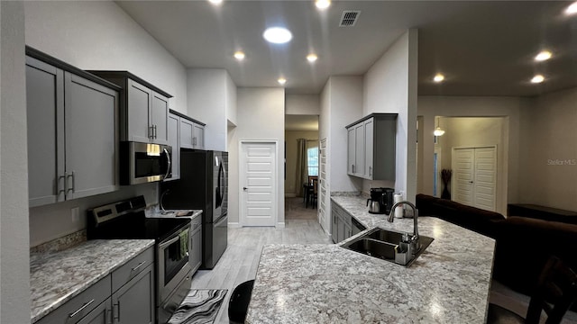 kitchen featuring stainless steel appliances, sink, a kitchen bar, light wood-type flooring, and gray cabinets