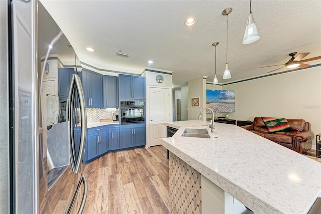 kitchen featuring light hardwood / wood-style flooring, sink, pendant lighting, black oven, and stainless steel fridge