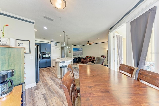 dining area featuring ceiling fan, sink, light wood-type flooring, and crown molding