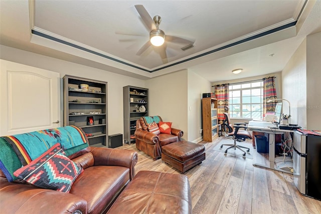 home office with built in shelves, hardwood / wood-style flooring, ceiling fan, and a tray ceiling