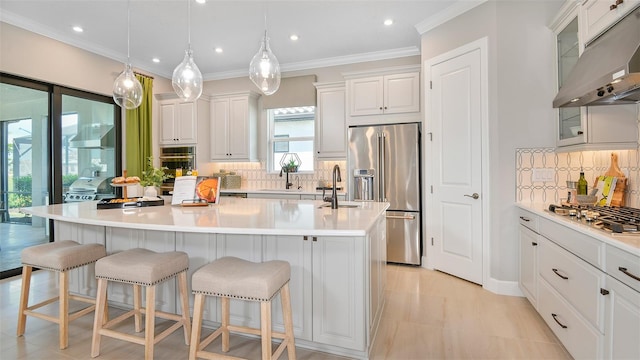 kitchen featuring a kitchen breakfast bar, stainless steel appliances, a kitchen island with sink, white cabinetry, and hanging light fixtures