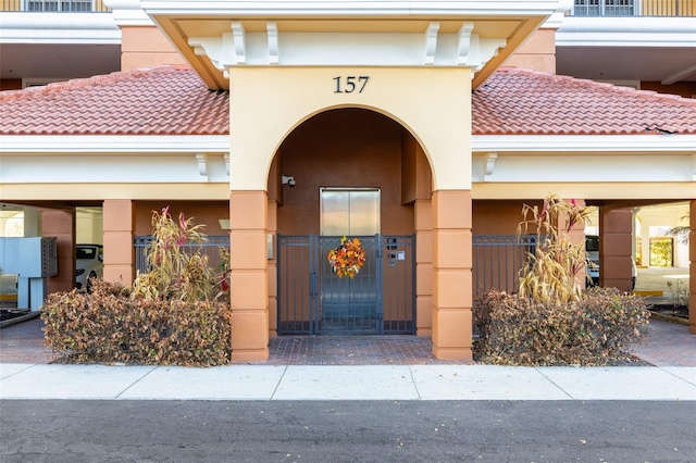 doorway to property featuring a gate, fence, stucco siding, and a tiled roof