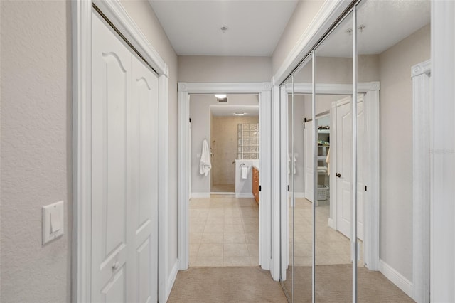 hall with baseboards, light carpet, and light tile patterned flooring