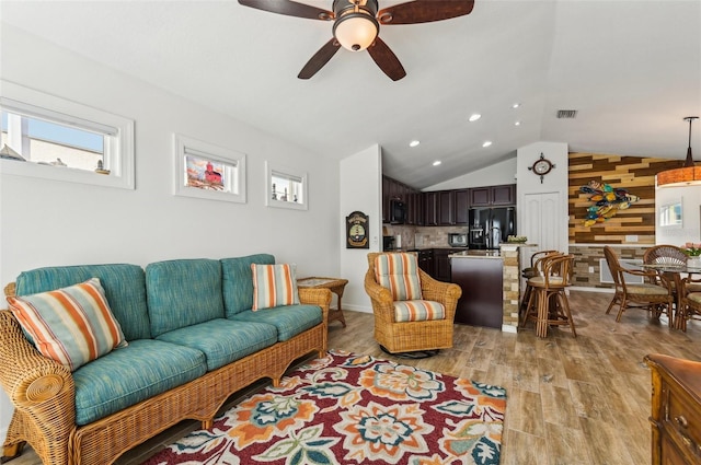 living room with light hardwood / wood-style floors, vaulted ceiling, wooden walls, and ceiling fan