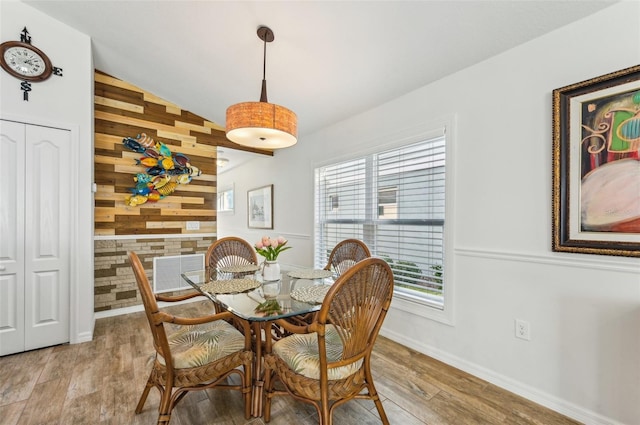 dining space with light hardwood / wood-style flooring, wood walls, a healthy amount of sunlight, and vaulted ceiling