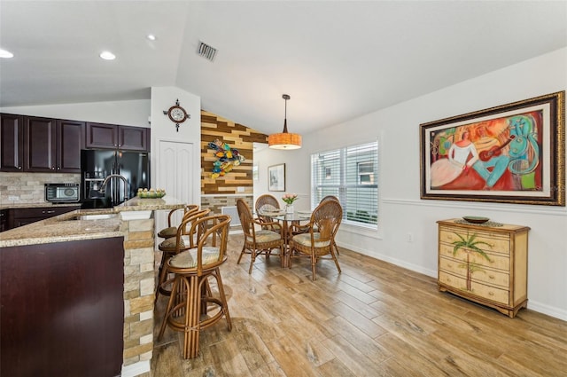 kitchen featuring lofted ceiling, wooden walls, light hardwood / wood-style flooring, black appliances, and pendant lighting