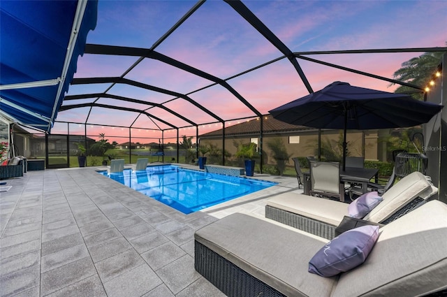 pool at dusk featuring glass enclosure and a patio area