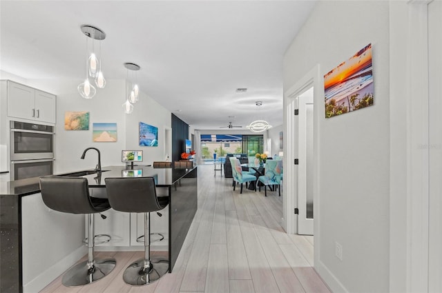 kitchen with pendant lighting, sink, light hardwood / wood-style flooring, ceiling fan, and double oven