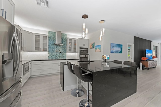 kitchen with backsplash, wall chimney exhaust hood, a breakfast bar, stainless steel appliances, and light hardwood / wood-style flooring