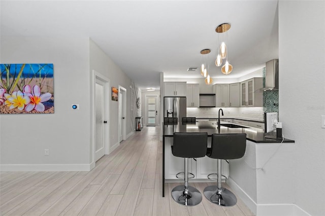 kitchen with decorative backsplash, sink, wall chimney range hood, pendant lighting, and light hardwood / wood-style flooring