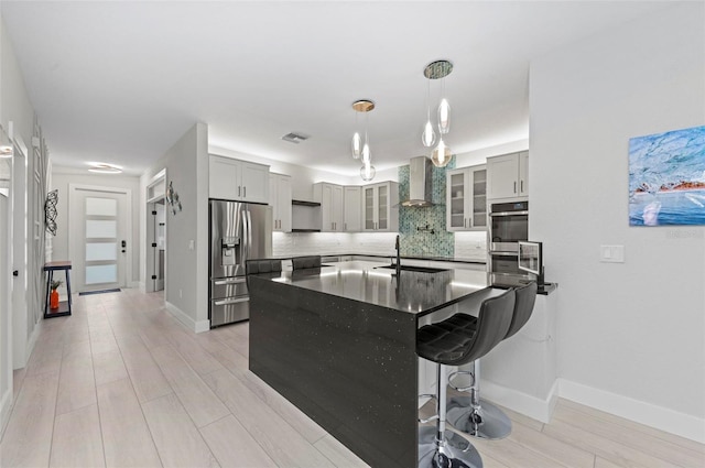 kitchen with wall chimney range hood, light hardwood / wood-style floors, decorative light fixtures, gray cabinets, and appliances with stainless steel finishes