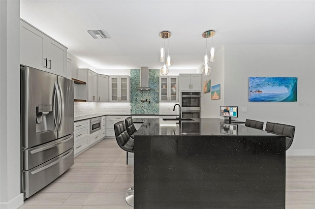 kitchen featuring a kitchen breakfast bar, sink, wall chimney exhaust hood, appliances with stainless steel finishes, and decorative light fixtures