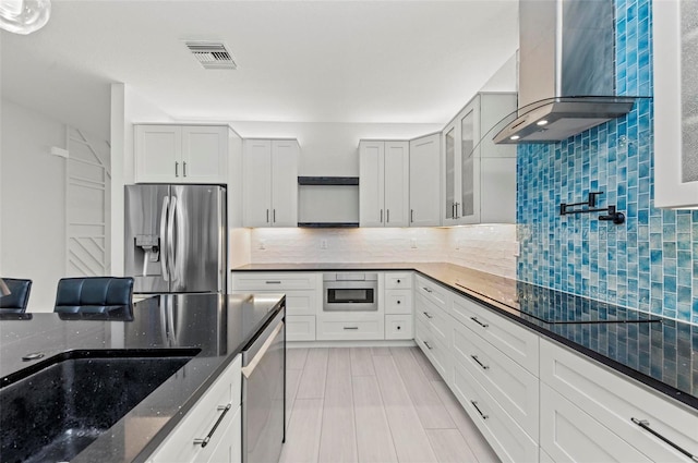 kitchen featuring white cabinets, wall chimney range hood, stainless steel appliances, and dark stone counters