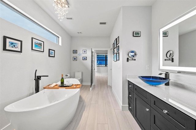 bathroom featuring vanity, an inviting chandelier, hardwood / wood-style floors, toilet, and a tub