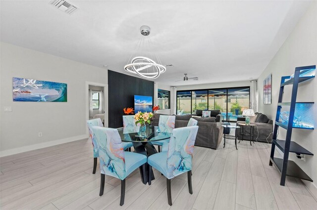 dining room with ceiling fan with notable chandelier and light hardwood / wood-style flooring