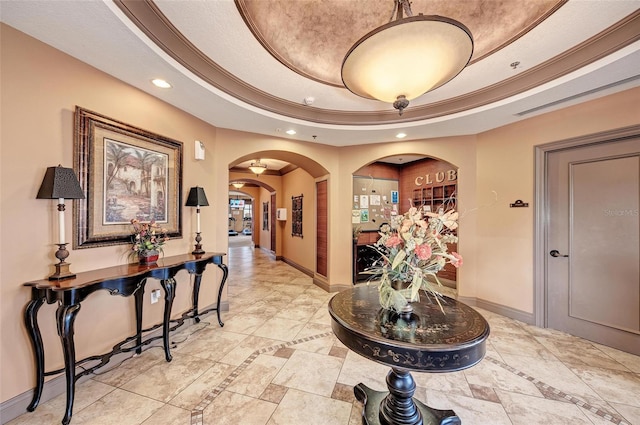 hall with a textured ceiling, a raised ceiling, and crown molding