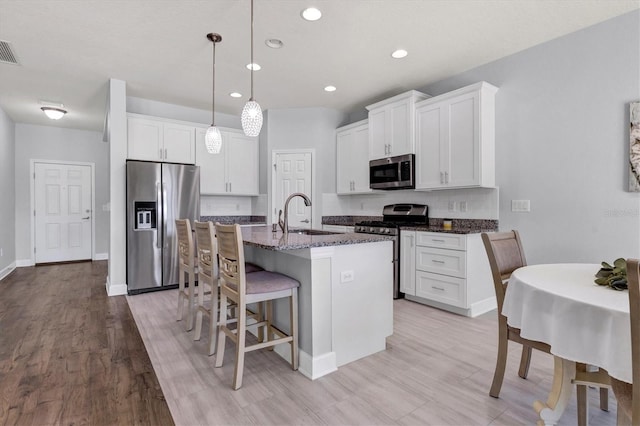 kitchen featuring appliances with stainless steel finishes, sink, an island with sink, white cabinetry, and dark stone countertops