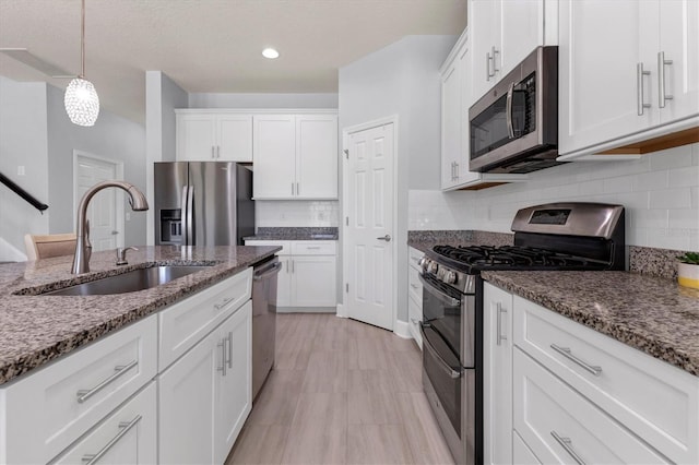 kitchen with sink, appliances with stainless steel finishes, decorative light fixtures, and white cabinets