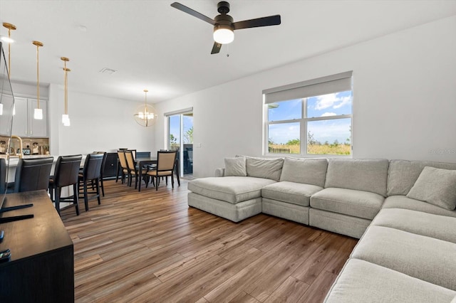 living room with ceiling fan with notable chandelier and hardwood / wood-style floors