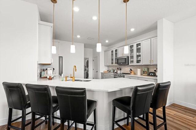 kitchen featuring kitchen peninsula, stacked washer / dryer, appliances with stainless steel finishes, white cabinetry, and sink