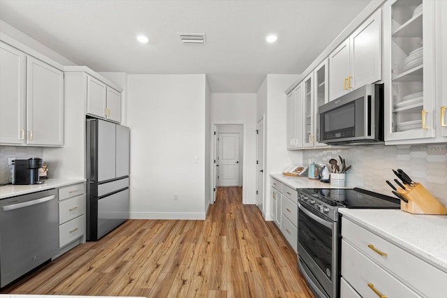 kitchen featuring backsplash, appliances with stainless steel finishes, light wood-type flooring, and white cabinets